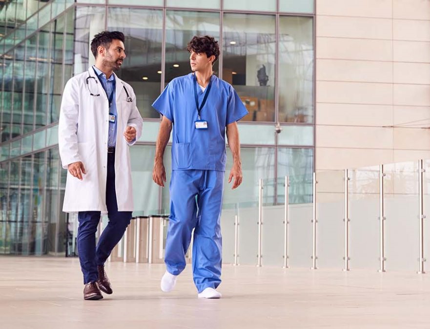 A nurse and doctor walking and talking outside of a hospital.
