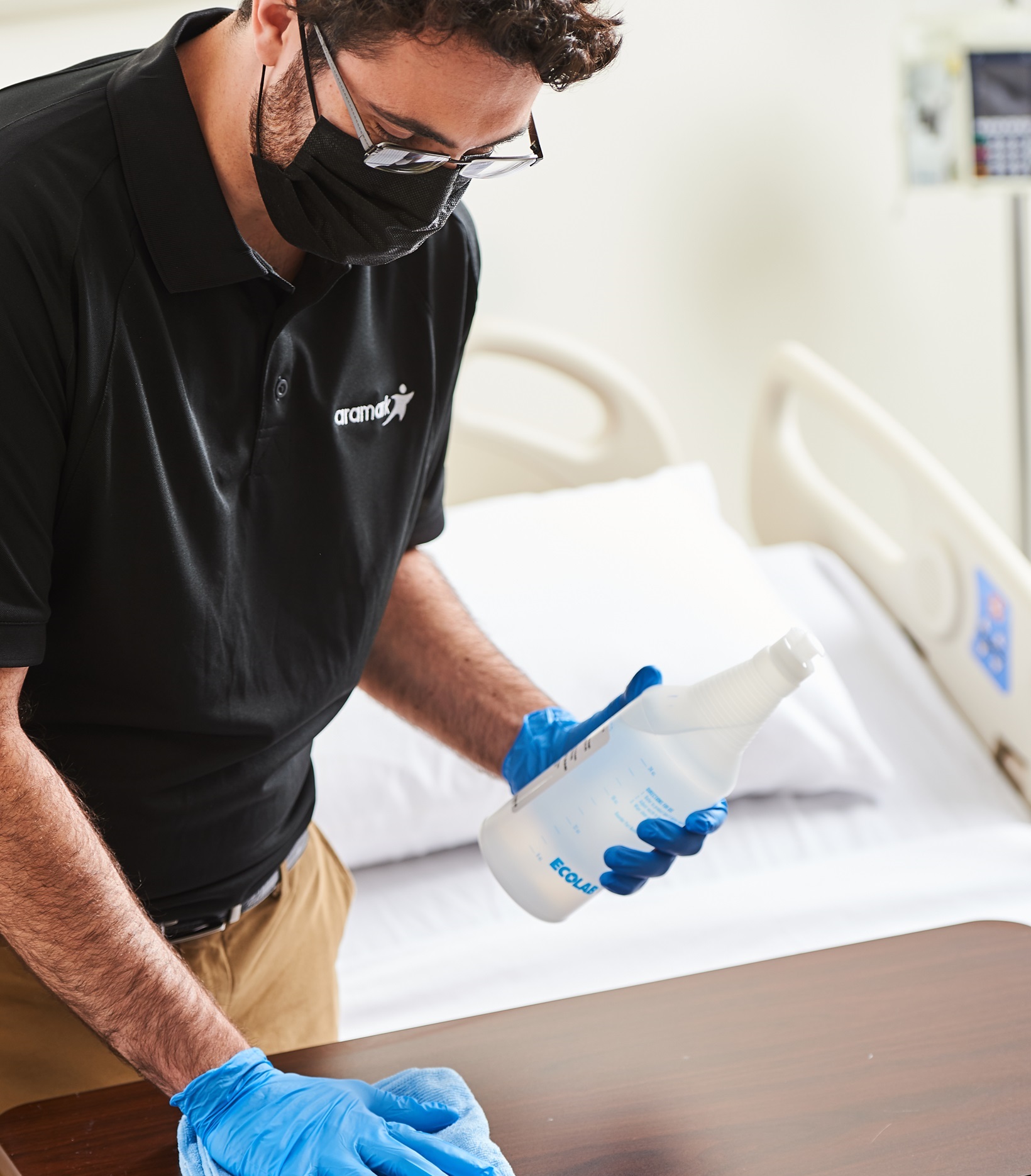 An Aramark employee wipes down the table in a hospital room with a disinfectant solution.