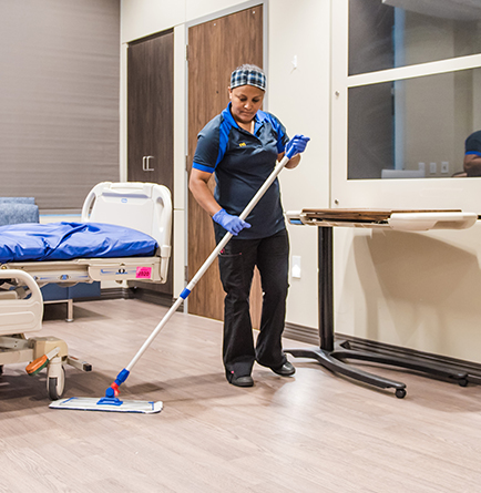 A healthcare employee using a mop to clean the floor of a hospital room.