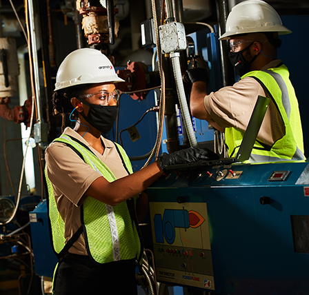 An Aramark employee wearing safety gear and a high-visibility vest doing maintenance on machinery.