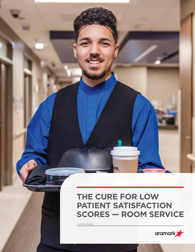 A hospital employee in a vest carrying a meal tray.