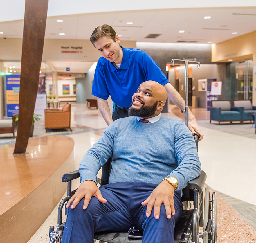 Hospital employee pushing a man in a wheelchair.