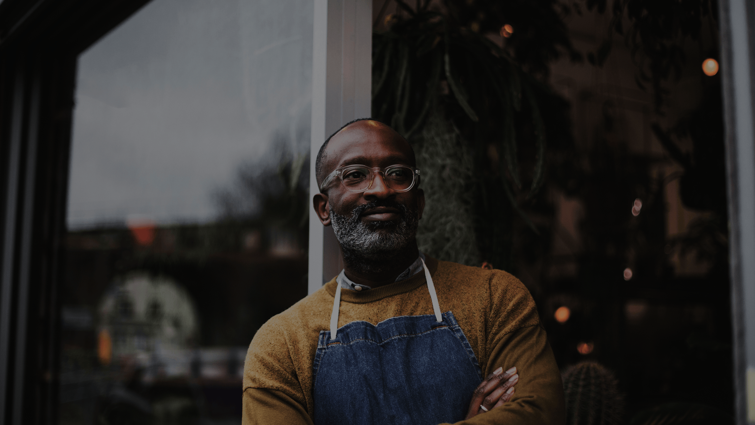 Older man wearing an apron stands in a doorway.