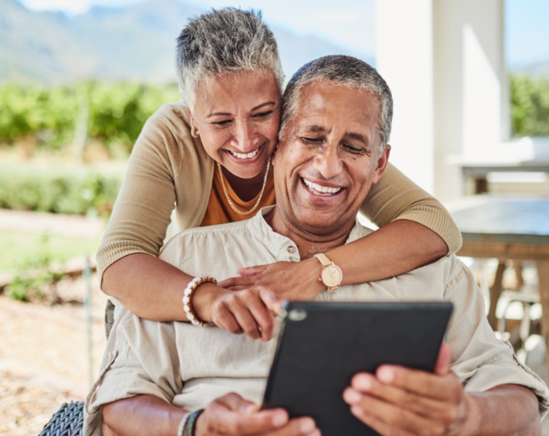 An affectionate older couple looks at a tablet.