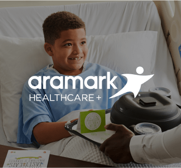Young patient smiling as his hospital meal is delivered, and the Healthcare+ logo..