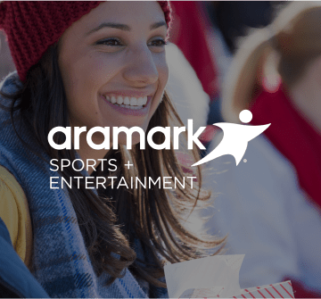 A spectator holding concessions, and the Aramark Sports + Entertainment logo.