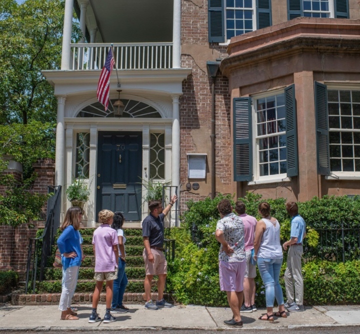 A tour guide talks to a group of people outside of a historic house.
