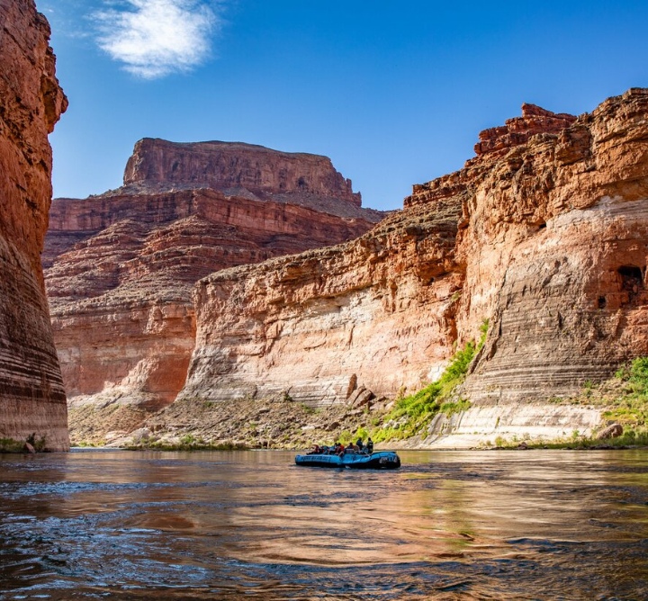 An inflatable boat rafting on the river through a canyon.