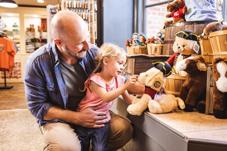 A father and young child looking at stuffed animals in a gift store.