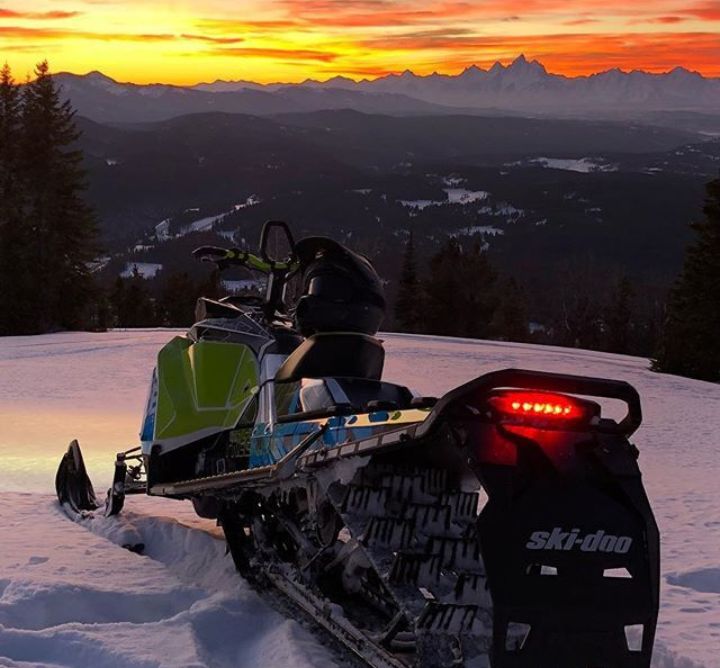 A snowmobile in the snowy mountains against a sunset.